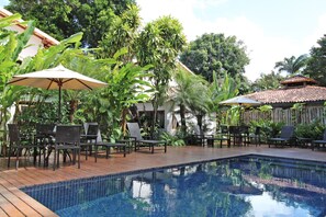 Un espace piscine avec une terrasse en bois, des chaises longues et des parasols.