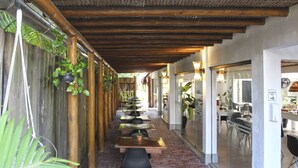 Un espace extérieur abrité, aménagé pour les repas, avec un sol en briques, des tables en bois et des chaises noires.