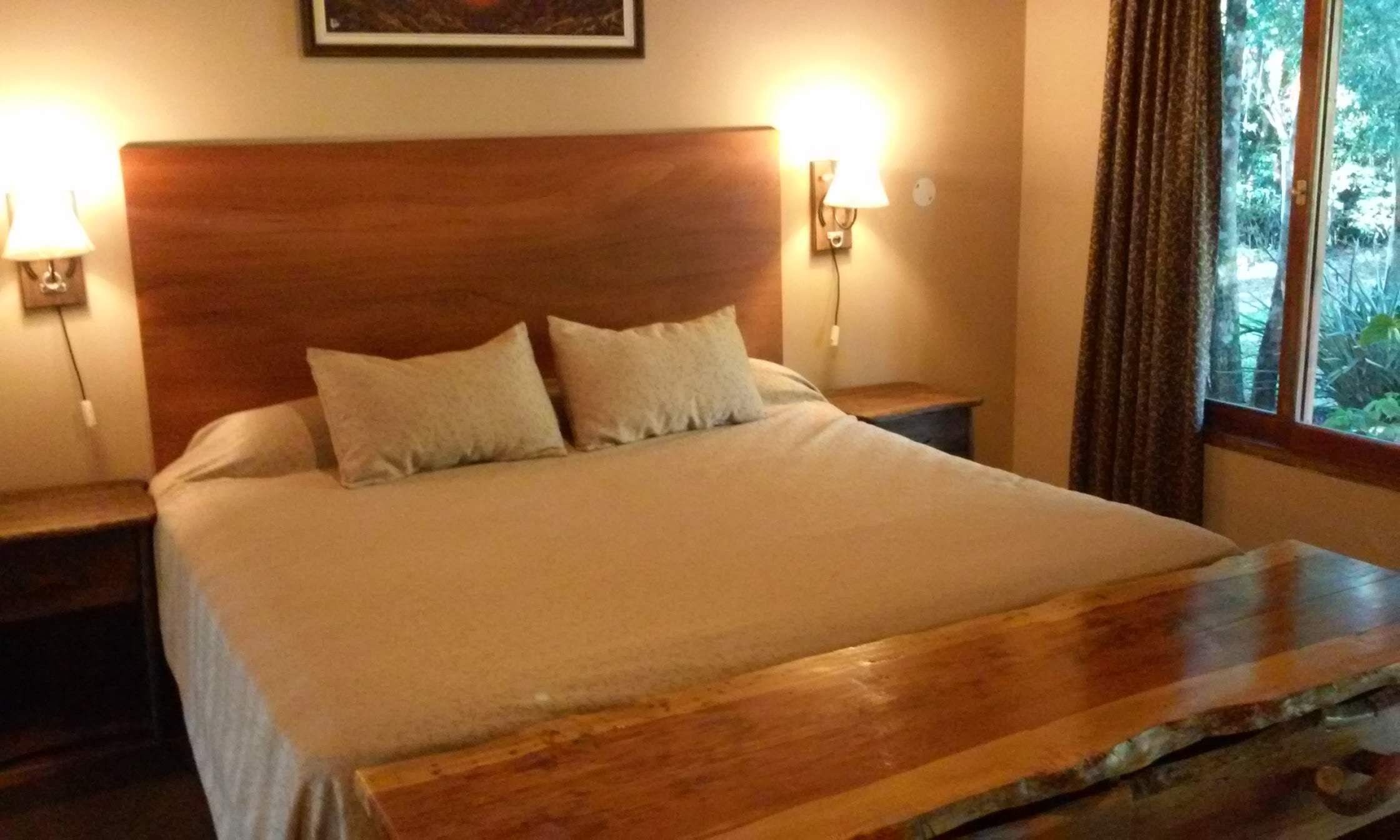 A neatly made bed with a wooden headboard, two bedside lamps, and a window with curtains.