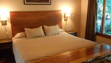 A neatly made bed with a wooden headboard, two bedside lamps, and a window with curtains.