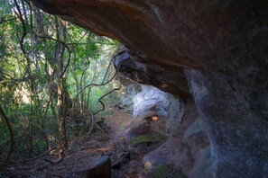 A natural cave formation with a rocky overhang and dense forest. - Ytororo Lodge (Dos de Mayo)