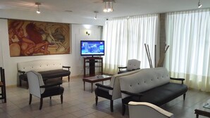 A living room with a sofa, chairs, a coffee table, a TV, and a painting on the wall. - Hotel Aoma Mar del Plata (Mar del Plata)