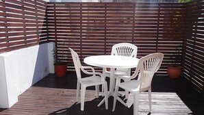 A patio with a round table and four white chairs, surrounded by a wooden fence and potted plants. - Hotel Aoma Mar del Plata (Mar del Plata)