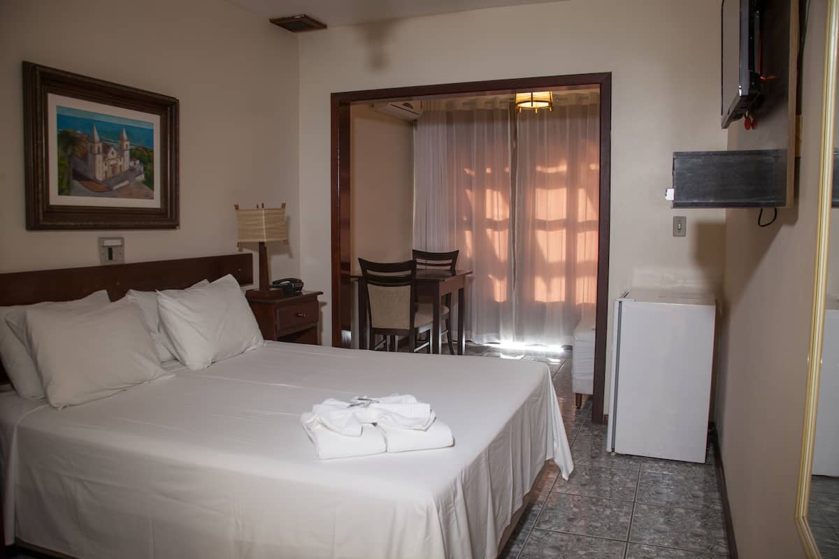 A hotel room with a bed, a desk, a chair, a television, and a refrigerator.