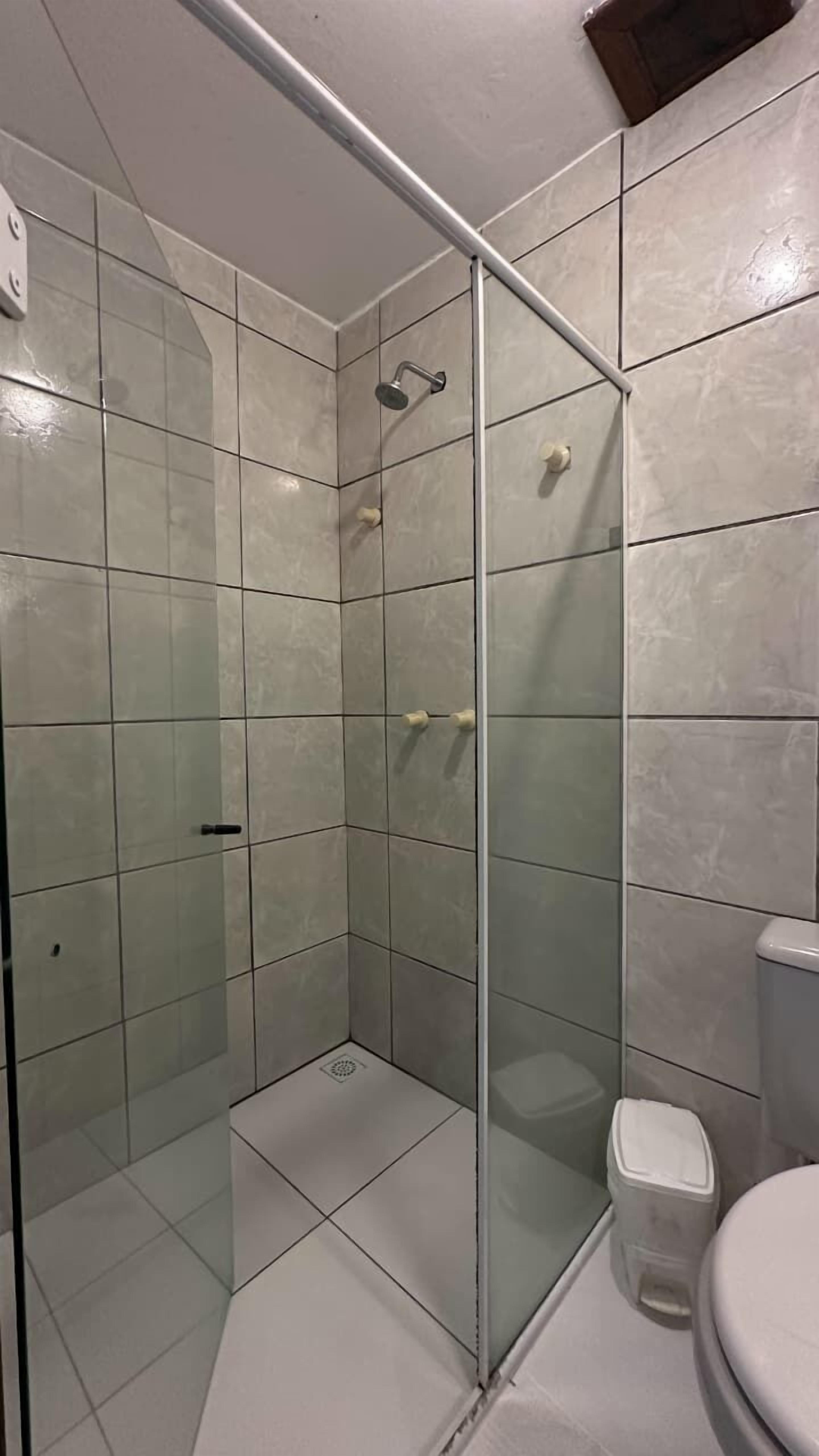 Ducha con puerta de cristal, inodoro y lavamanos en un baño con paredes y suelo de azulejos.