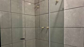 Ducha con puerta de cristal, inodoro y lavamanos en un baño con paredes y suelo de azulejos.