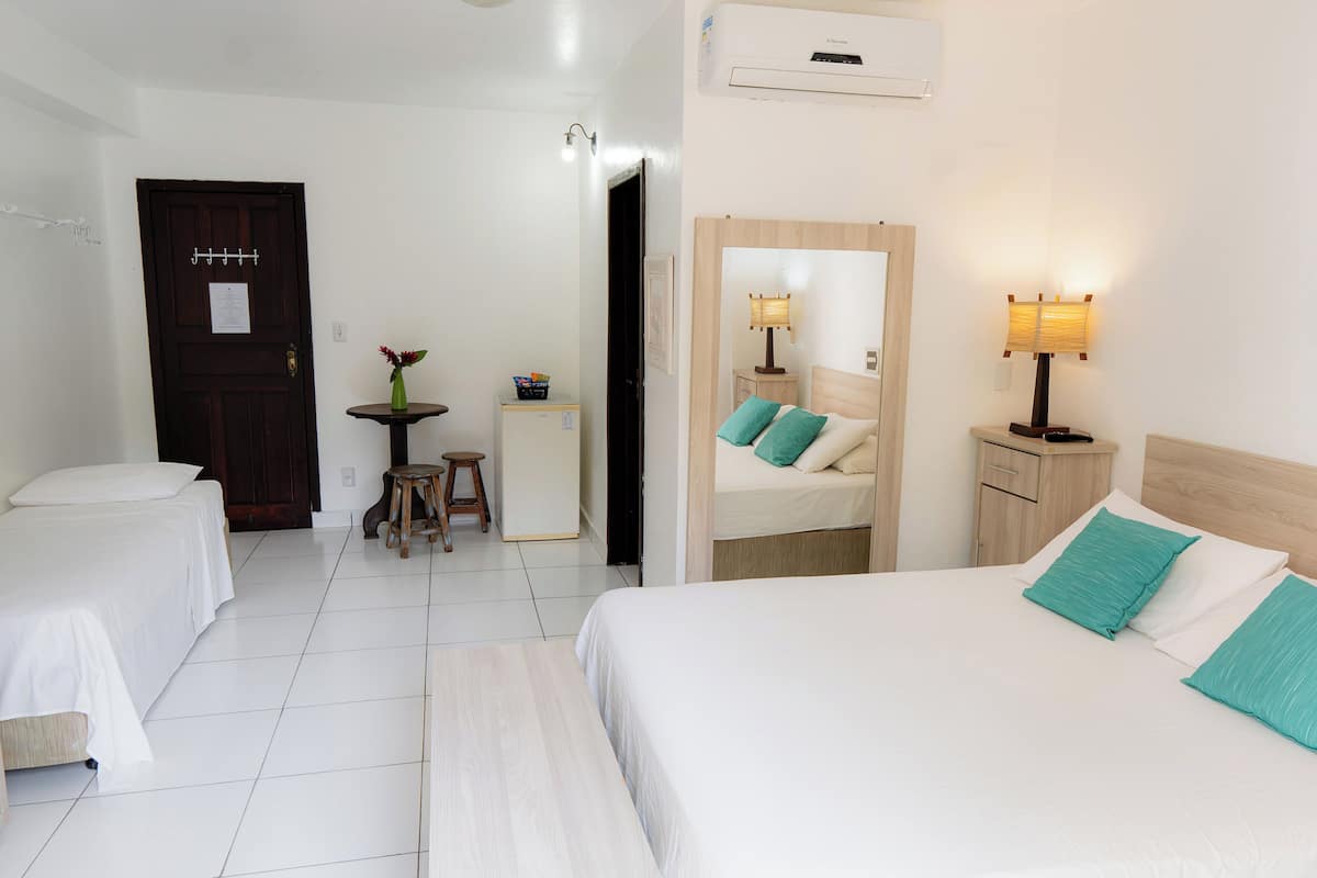 A hotel room with two beds, a small table with a lamp, a mirror, and a door.