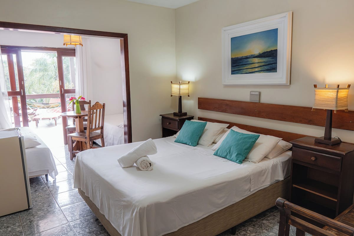 A hotel room with a bed, a nightstand, a desk with a chair, a window, and a painting on the wall.