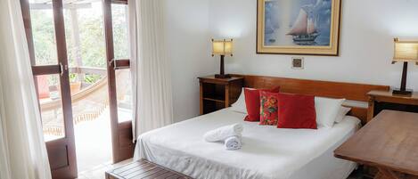 Habitación de hotel con cama, banco, mesa, un cuadro y vistas al exterior.