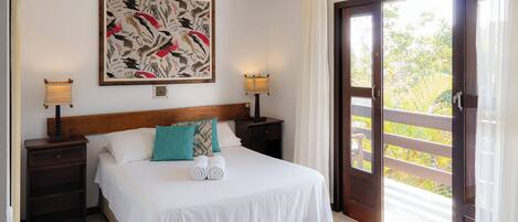 A hotel room with a bed, two bedside tables, a wall-mounted lamp, a painting, and a sliding glass door to a balcony.