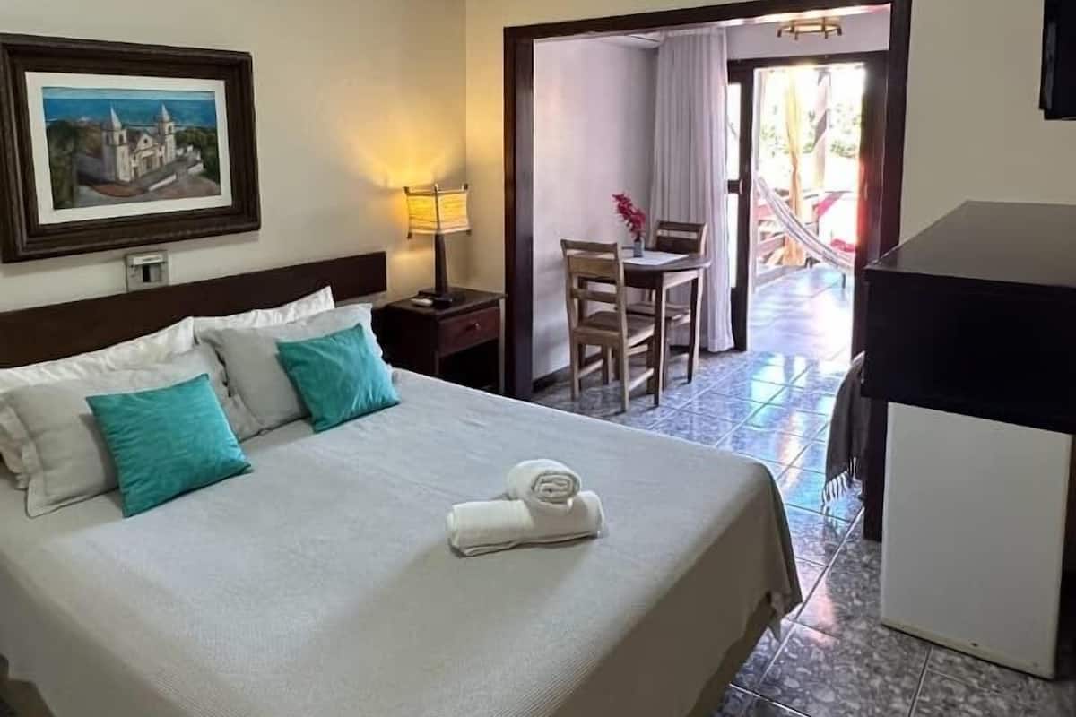 A hotel room with a bed, a desk, a chair, a lamp, and a painting on the wall.