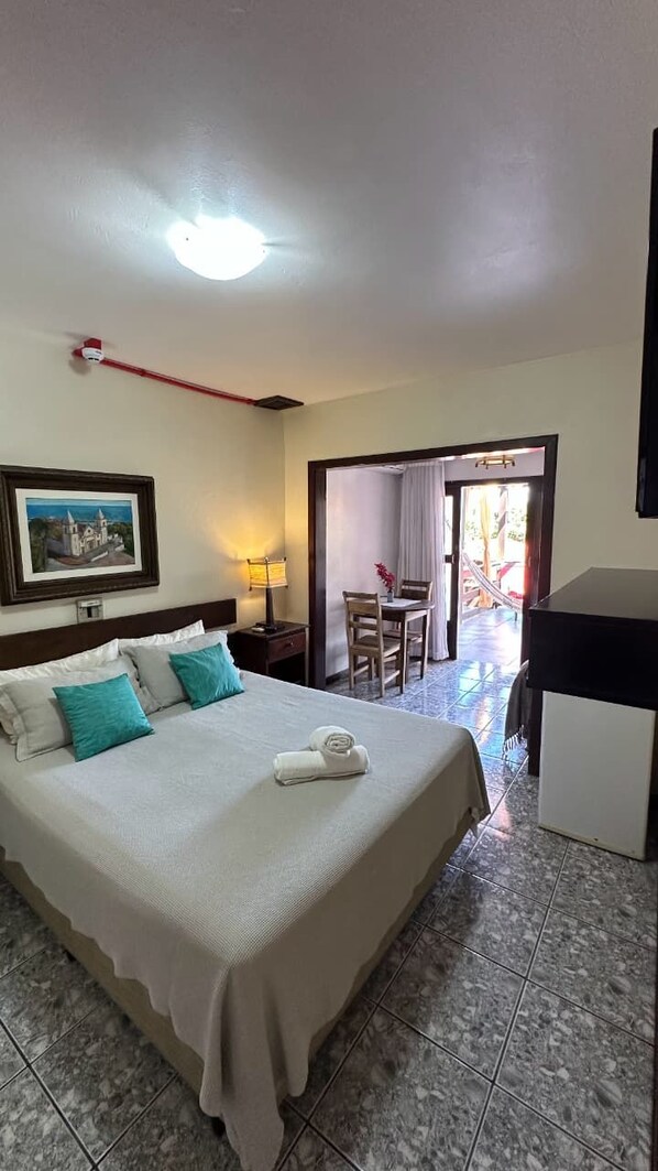 Habitación de hotel con cama, escritorio, silla, lámpara y un cuadro en la pared.