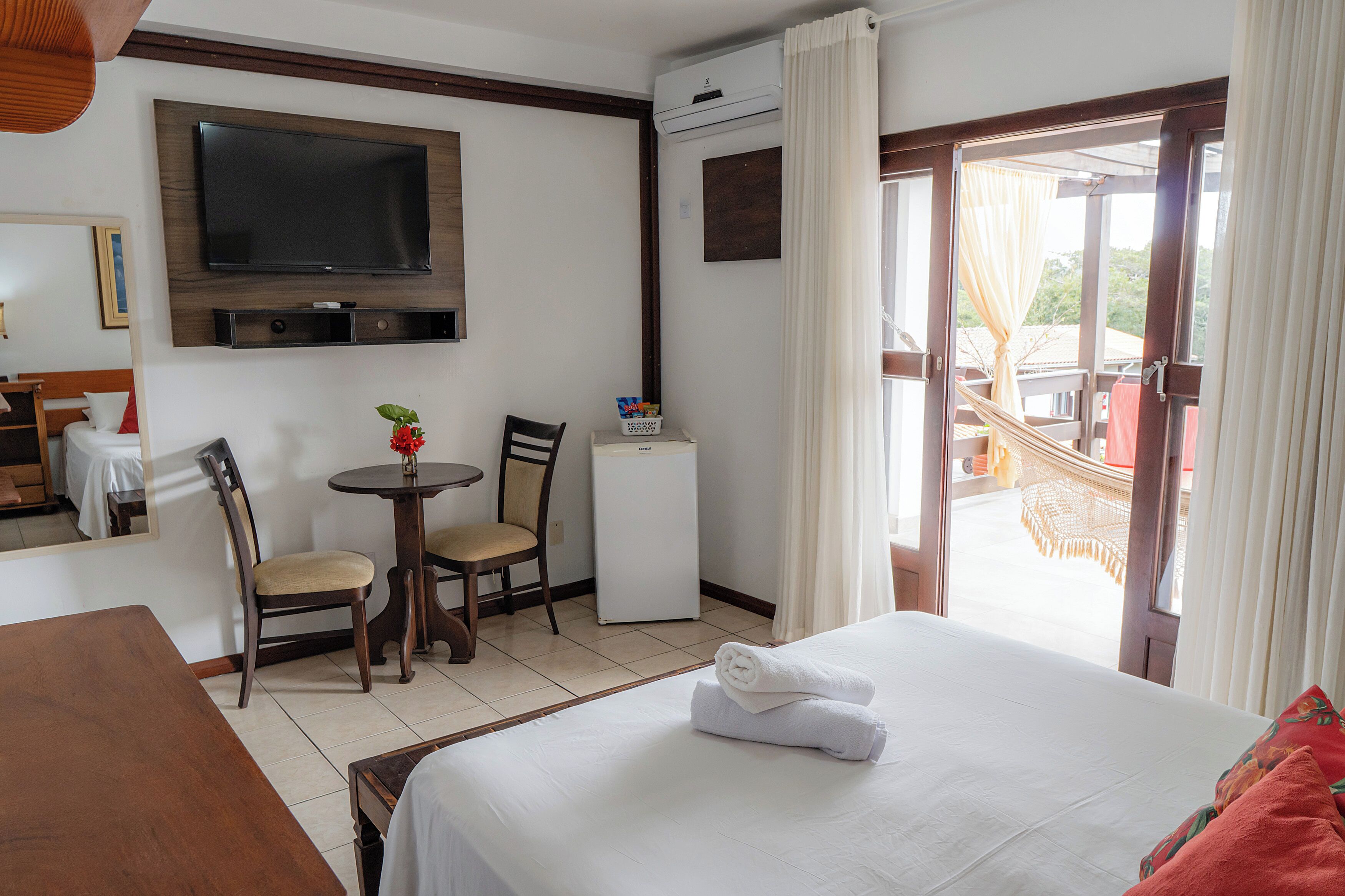A hotel room with a bed, a TV, a desk, a chair, a small table, and a balcony with a view.