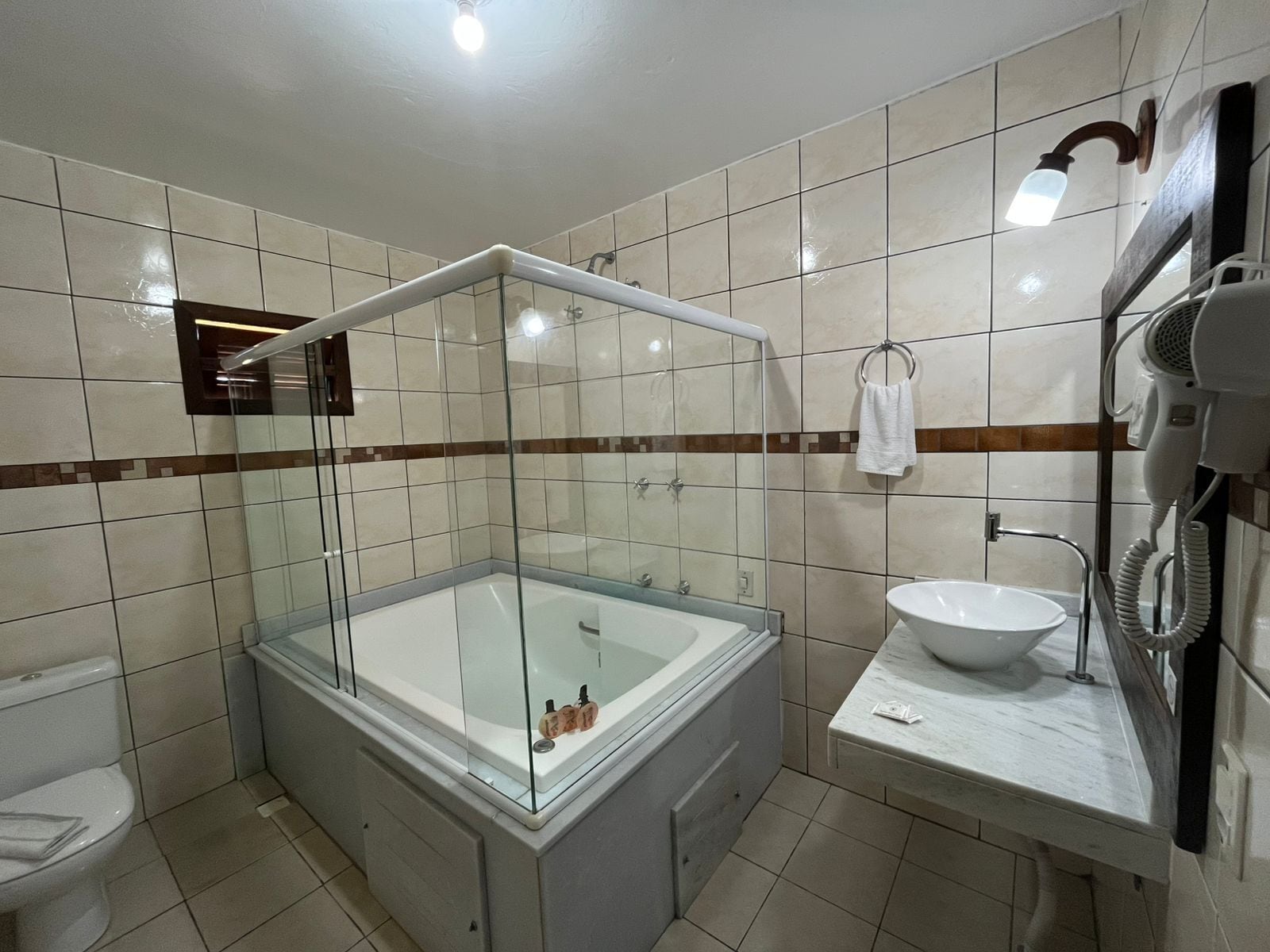 Un baño moderno con una bañera de hidromasaje con mampara de vidrio, un lavabo y un secador de pelo.