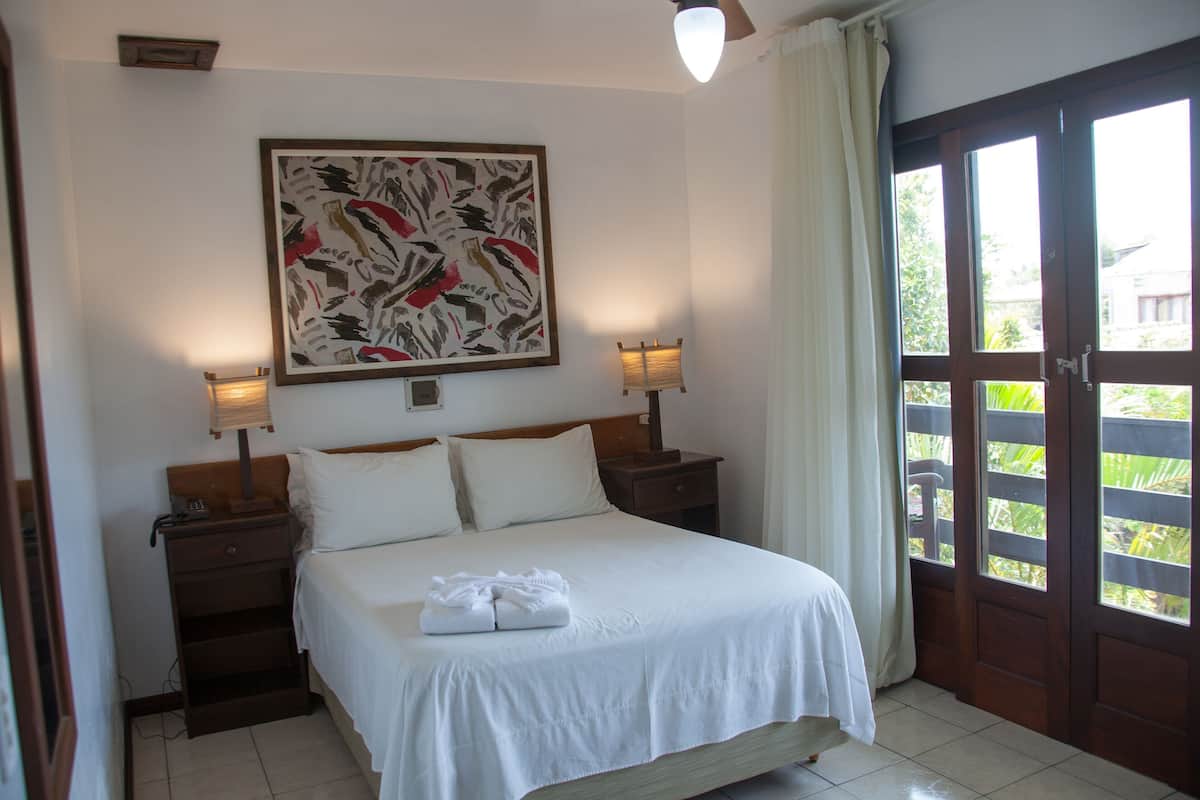 A hotel room with a bed, two bedside tables, a wall-mounted lamp, a door with a view, and a large abstract painting.