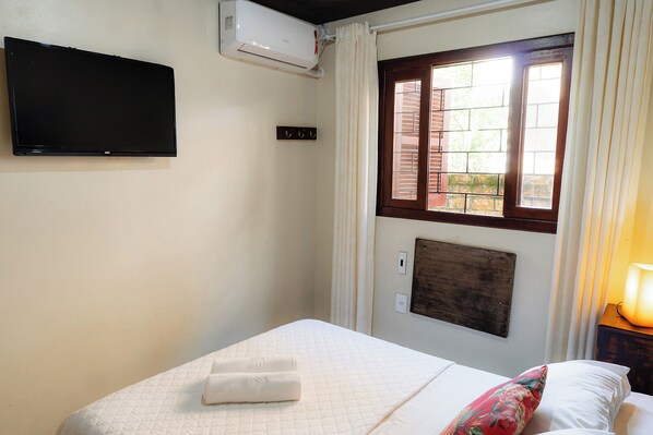 Habitación de hotel con cama, televisión de pantalla plana en la pared, ventana con cortinas y calefactor en la pared.