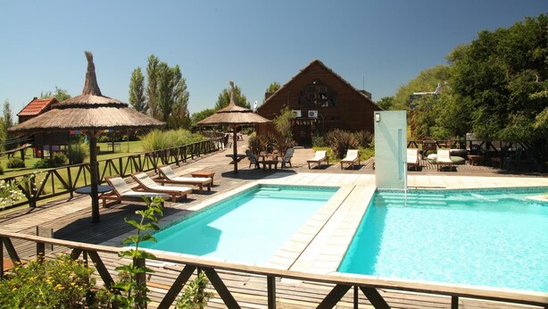A pool area with lounge chairs, a wooden deck, and a building with a thatched roof. - Paso del Tigre (Santa Fe)