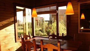 A wooden dining area with a table and chairs, large windows with curtains, and hanging pendant lights. - Paso del Tigre (Santa Fe)