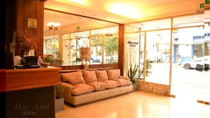 A hotel lobby with a reception desk, a sofa, and large windows offering a view of the street. - Hotel Mar Azul (Mar del Plata)