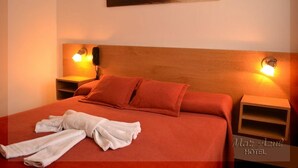 A neatly made bed with red bedding and two pillows, a white towel, and a wooden headboard. There are two bedside tables with lamps, and a painting above the bed. - Hotel Mar Azul (Mar del Plata)