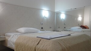 A hotel room with a bed, a bedside table, a mirror, and a wall-mounted light fixture. - Hotel Premier (Campo Grande)