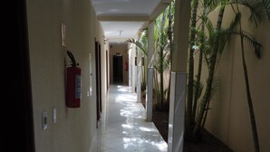 A corridor with tiled flooring, a fire extinguisher, and potted plants along the walls. - Hotel Premier (Campo Grande)