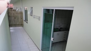 A narrow corridor with a tiled floor, a wooden fence on one side, and a glass door leading to a kitchen area with cabinets and a countertop. - Residencial Floripamar 2 (Florianópolis)