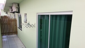 A corridor with a tiled floor, a wooden fence, and a sliding glass door with a green curtain. - Residencial Floripamar 2 (Florianópolis)