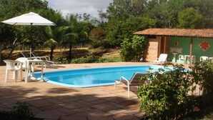 Una piscina con lettini e ombrellone, circondata dal verde e da un piccolo edificio con tetto in tegole.