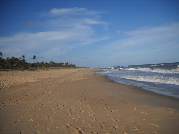 A wide sandy beach with footprints leading to the water, palm trees in the background, and a clear sky. - Pousada Refúgio do Corsário (Mata de São João)