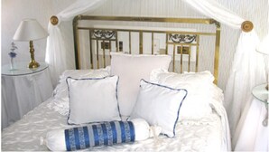 Uma cama com dossel, roupa de cama branca e almofada listrada em azul.