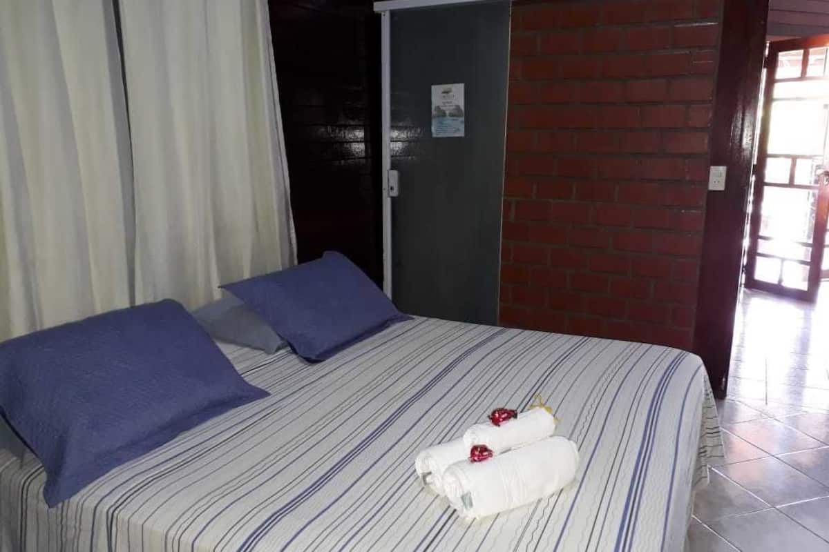 Quarto de hotel com uma cama, duas almofadas, uma porta e uma parede de tijolos.