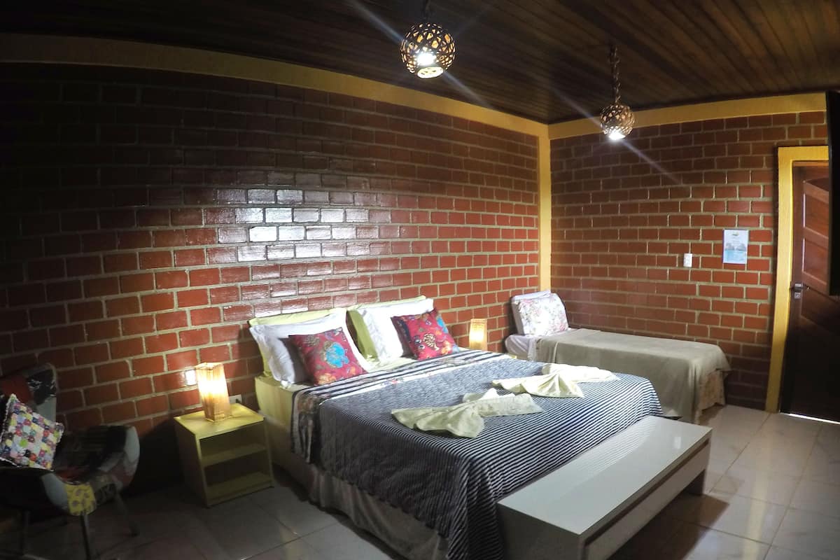 Quarto com parede de tijolos, cama com roupa de cama listrada, mesa de cabeceira e criado-mudo.