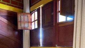 A corner room with a brick wall, a wooden door, a window with curtains, and a blue chair. - Pousada Ilha Bela (Fernando de Noronha)