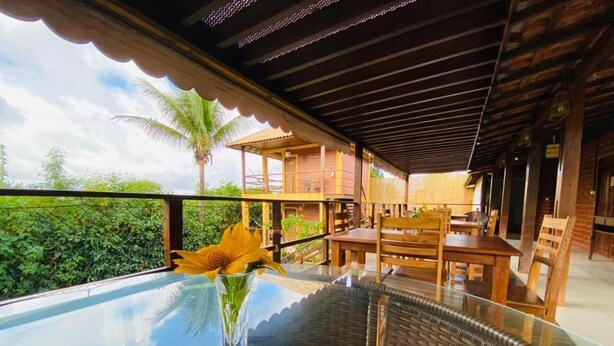 A glass-top dining table with colorful cushions, a vase with a yellow flower, and a view of the outdoors. - Pousada Ilha Bela (Fernando de Noronha)