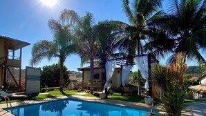 Une piscine avec une terrasse carrelée, entourée de palmiers et d’un bâtiment à la façade également recouverte de carreaux.