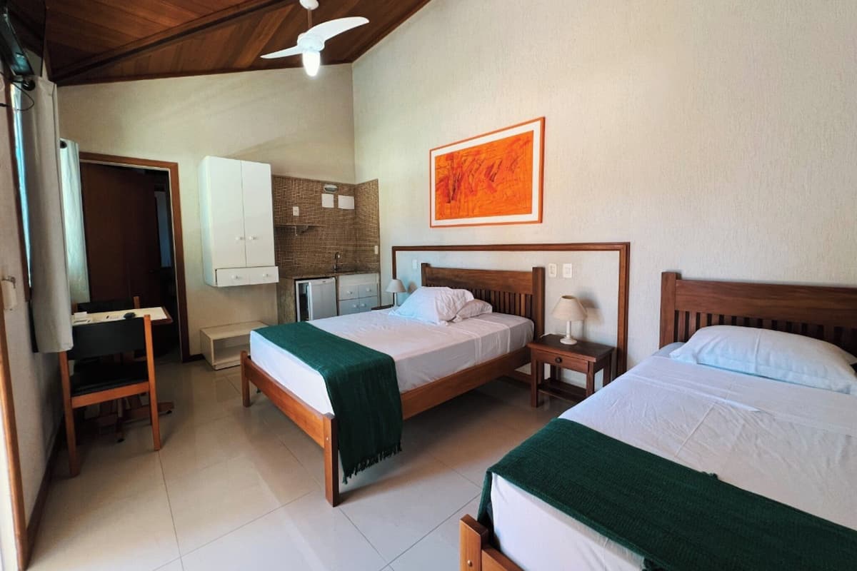 A hotel room with two beds, a desk, a chair, a ceiling fan, and a bathroom.
