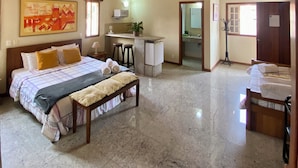 Une chambre spacieuse avec un grand lit, un banc, une petite kitchenette et une salle de bain.