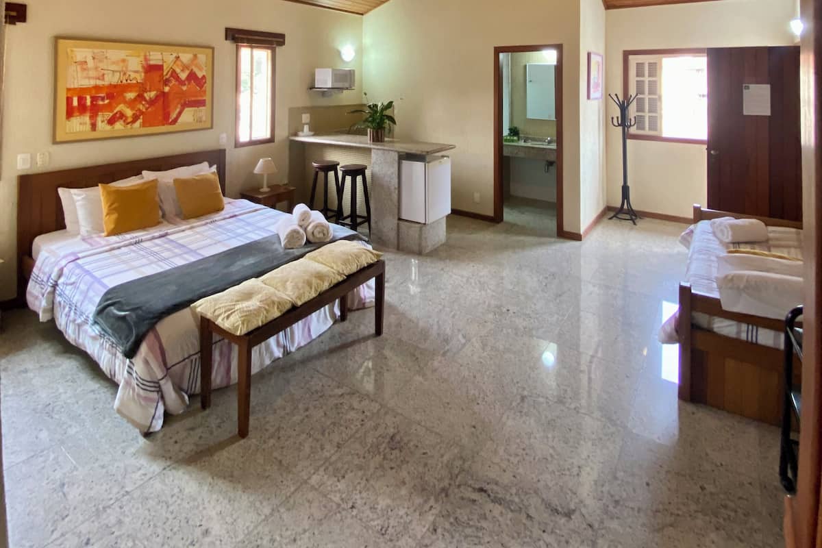 A spacious bedroom with a large bed, a bench, a small kitchenette, and a bathroom.