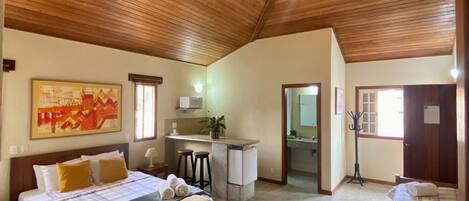 A spacious bedroom with a large bed, a bench, a small kitchenette, and a bathroom.