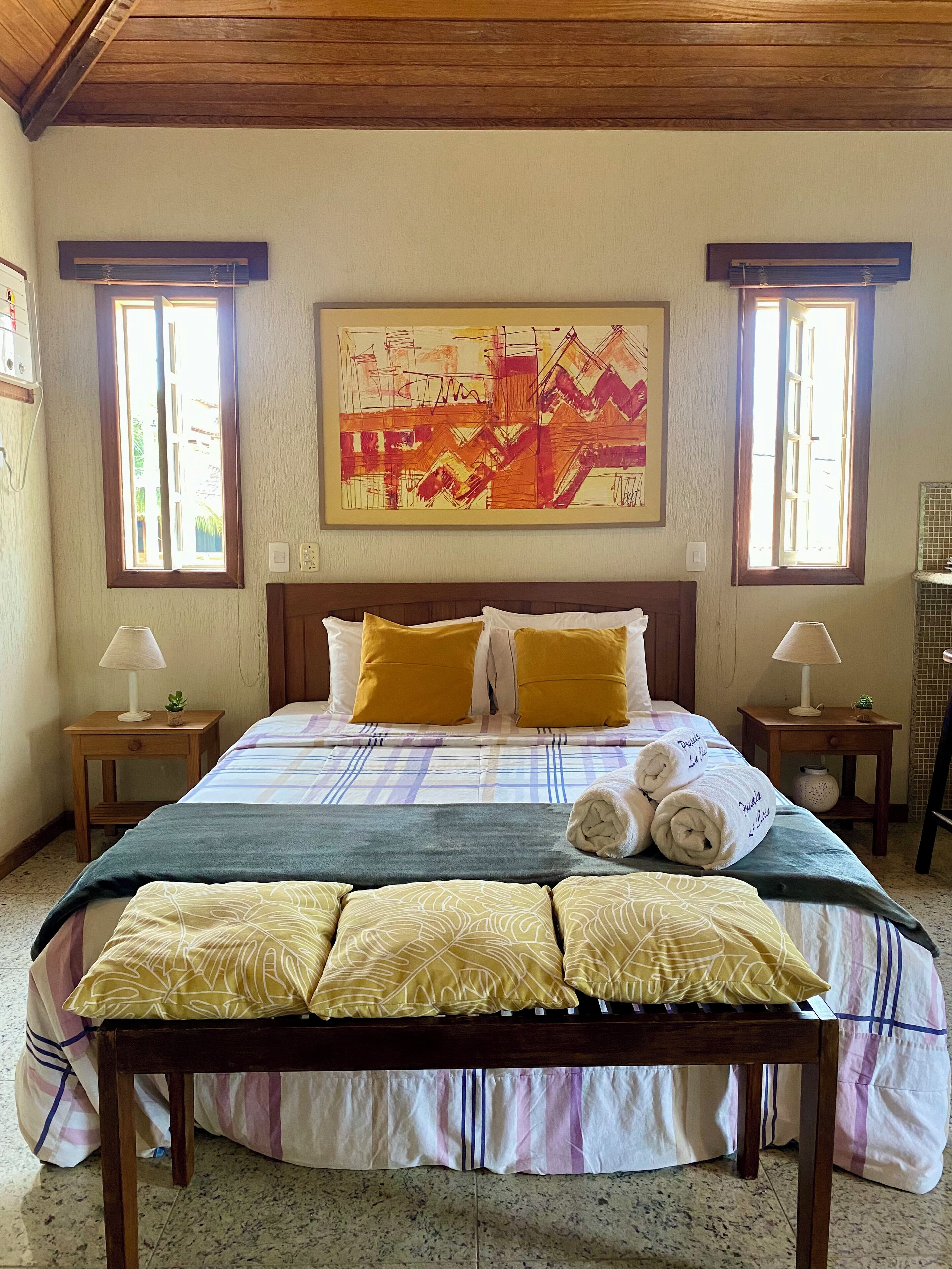 A neatly made bed with a checkered bedspread, two pillows, and two rolled towels.