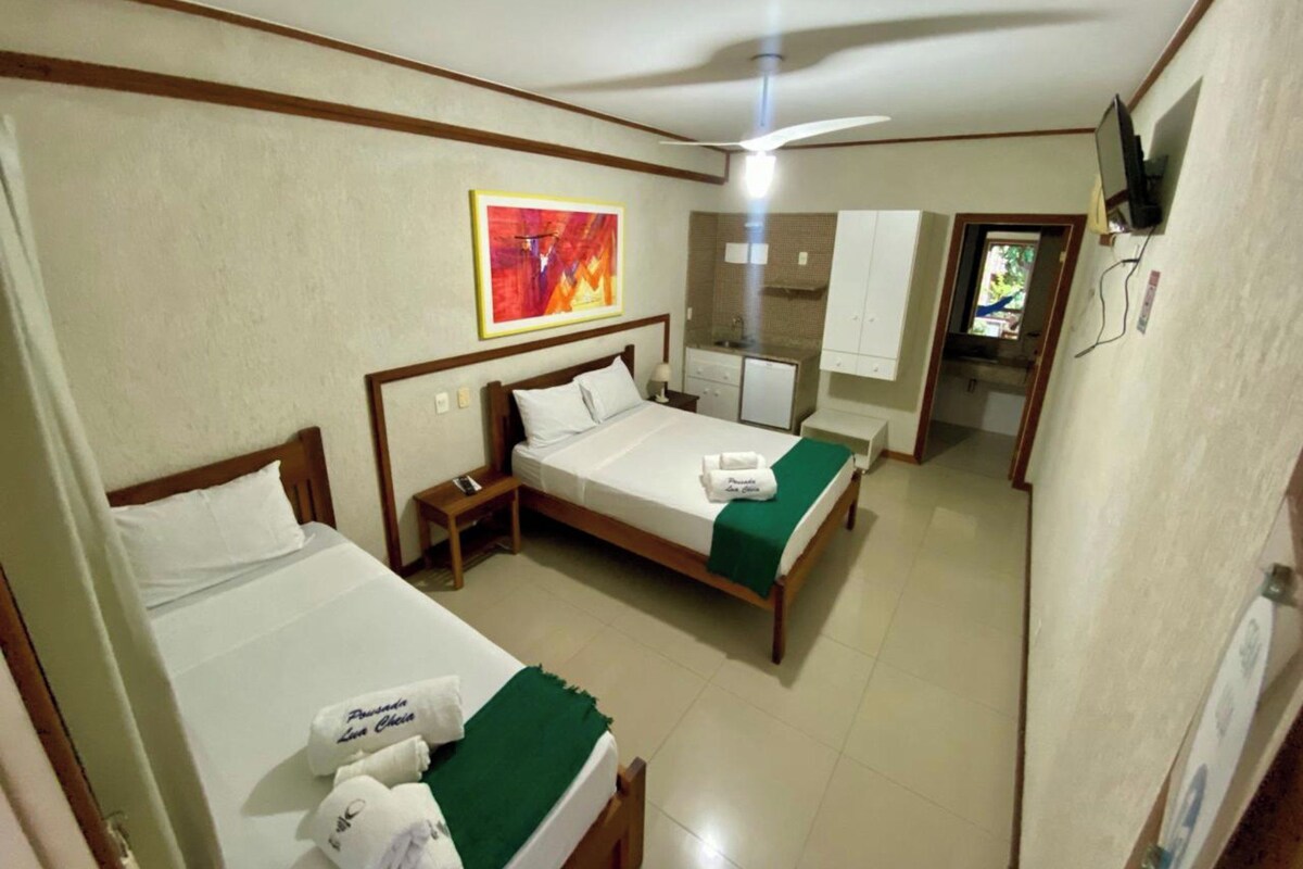 A hotel room with two beds, a small kitchenette, a television, and a painting on the wall.