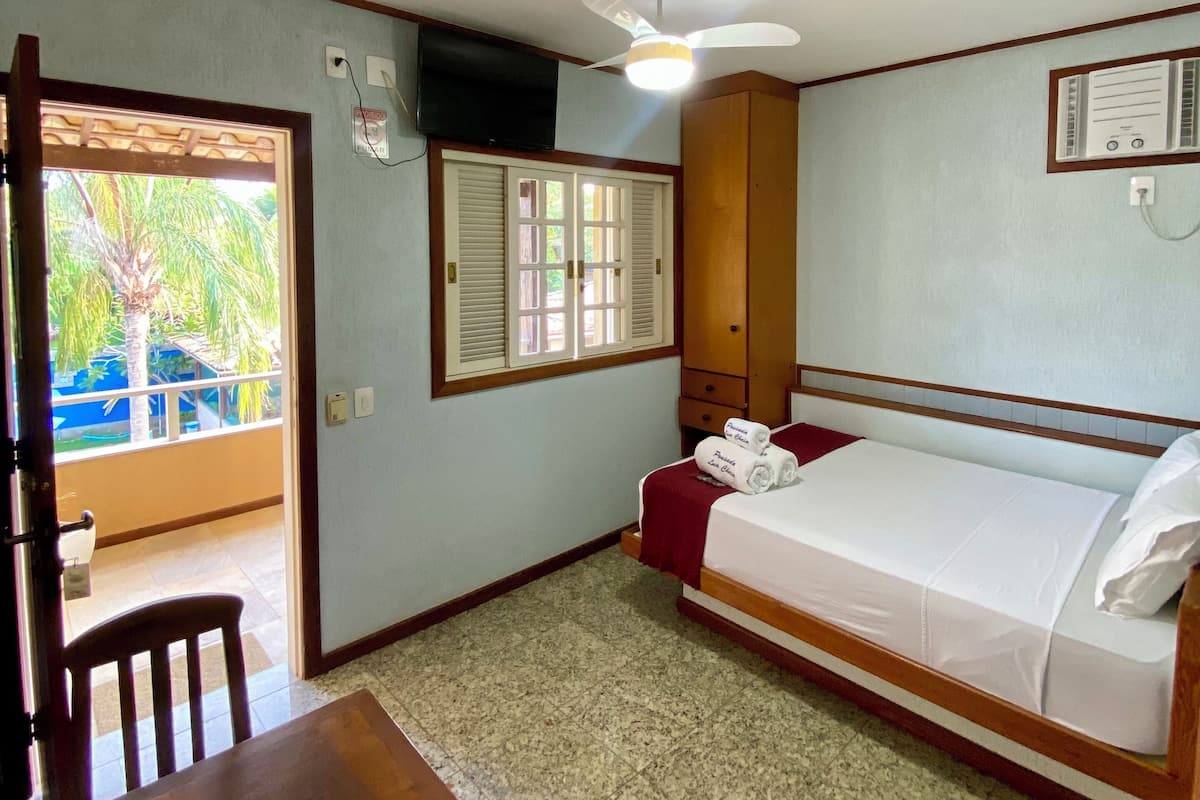 A small, clean room with a bed, a table, and a ceiling fan.