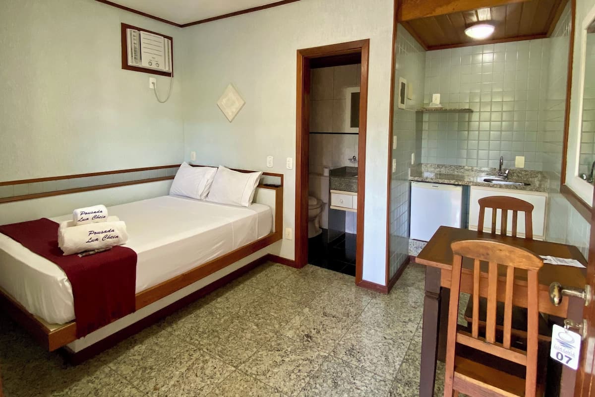 A compact room with a bed, a small table, and a chair. There is a kitchenette with a sink and a stove.