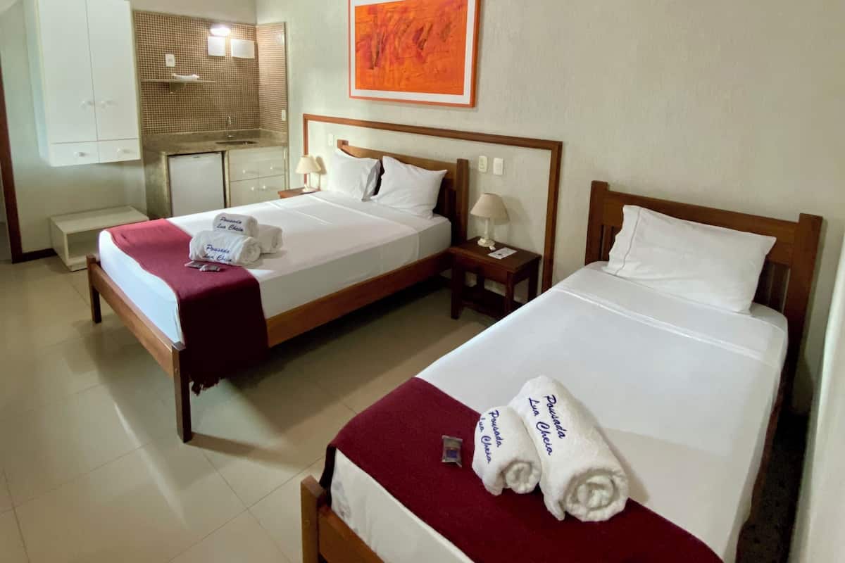 A hotel room with two beds, a wooden ceiling, a framed artwork on the wall, and a bathroom with a mirror and towel rack.