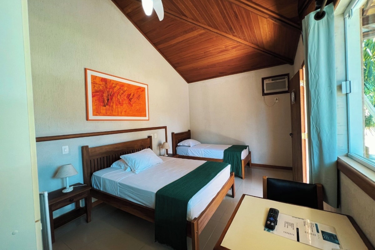A room with two beds, a table with a remote control, a lamp, and a ceiling fan.