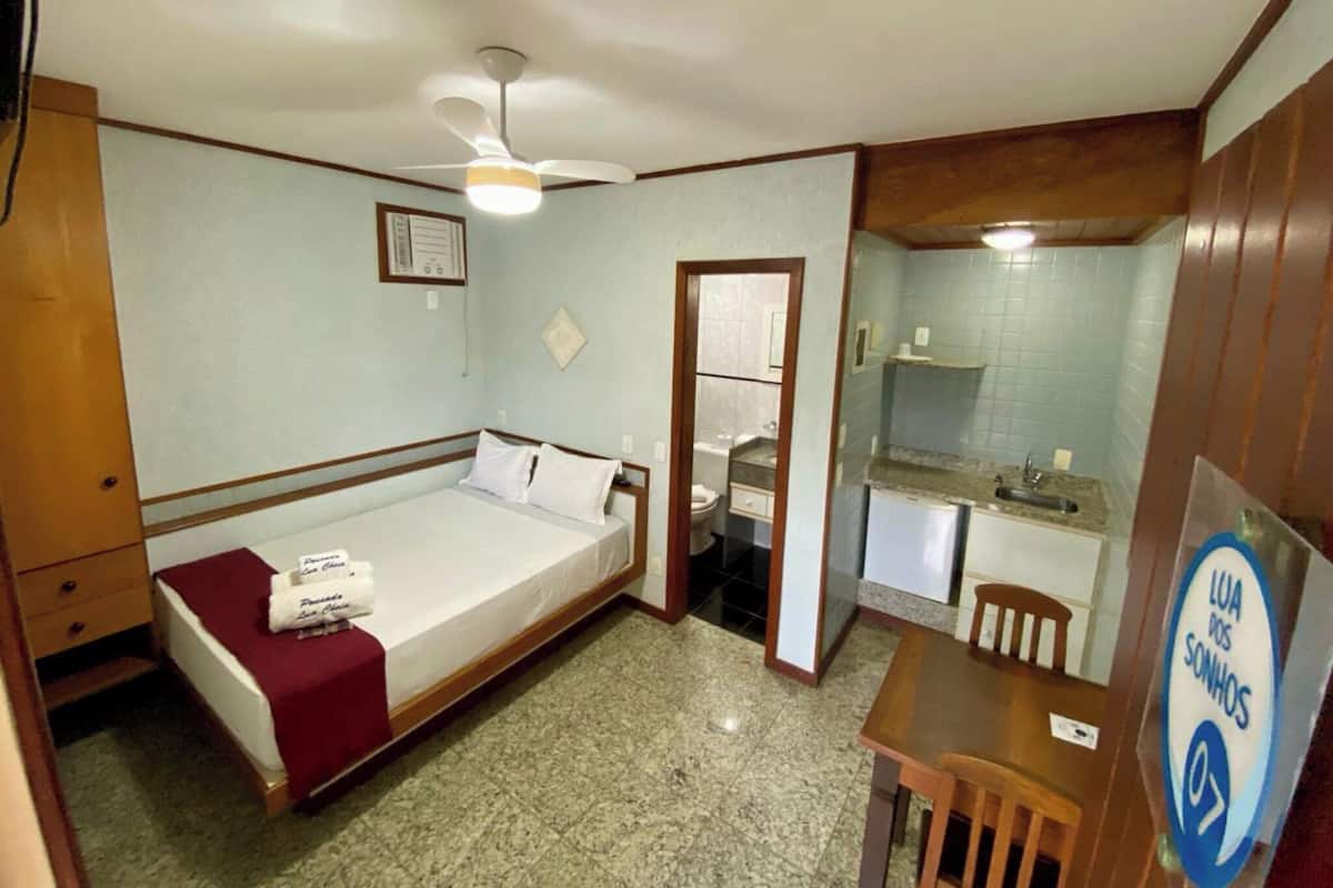 A compact room with a bed, a small kitchenette, a ceiling fan, and a sign indicating room number 07.