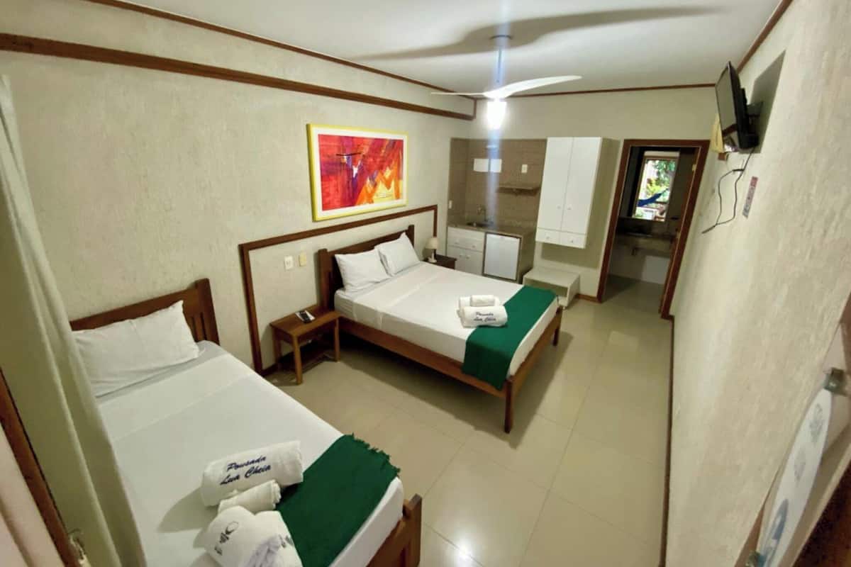 A hotel room with two beds, a small kitchenette, a television, and a painting on the wall.