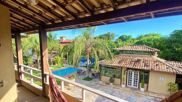 Un balcon avec un hamac, une piscine et une vue sur une maison dont le toit est recouvert de tuiles.