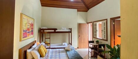 A bedroom with a wooden ceiling, a bed with a mattress and pillows, a bedside table, a wall-mounted artwork, and a small table with chairs.